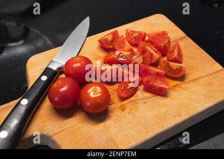 Holzschneidebrett mit einem kleinen Messer und Kirschtomaten vierteln auf der Oberseite geschnitten. Schneiden von Tomaten für Salat, weichen Fokus Stockfoto