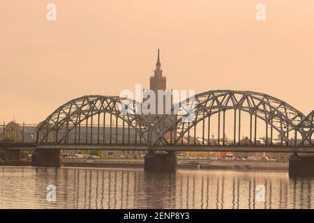 Blick auf die Lettische Akademie der Wissenschaften, die Eisenbahnbrücke und den Daugava-Fluss bei Sonnenaufgang in Riga, Lettland Stockfoto