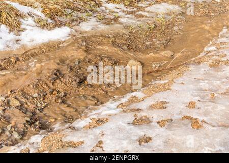 Ländliche Landstraße bedeckt mit schmelzendem Schnee und Schlamm an einem frühen Frühlingstag in der Tschechischen Republik. Schlammige Straße in der Landschaft. Geschmolzener Schnee. Stockfoto