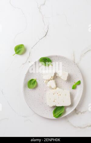 Feta-Käse mit Basilikumblättern auf dem Teller und weißem Hintergrund. Stockfoto