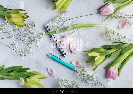 Arbeitsbereich mit Tagebuch, Notizbuch, Stift, Blumen auf hellblauem Hintergrund. Schreibtisch im Home Office. Draufsicht femininer Hintergrund. Flach liegend, Draufsicht. Stockfoto