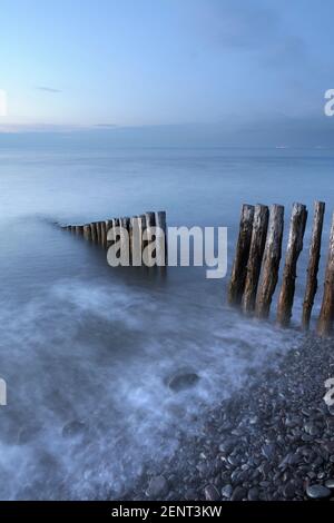 Flut waschen über Felsen und hölzernen Buhnen am Bossington Strand, Somerset, UK. Stockfoto