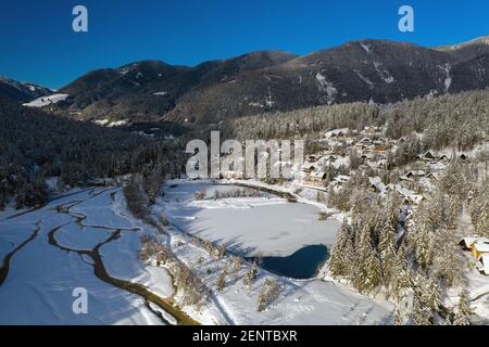 Luftaufnahme des Sees Jasna in Kranjska gora. Drohne bewegt sich über Tal mit schneebedeckten Kiefernwald. Stockfoto