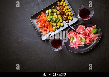 Prosciutto mit verschiedenen Vorspeisen mit einem Glas Rotwein auf schwarzem Hintergrund. Über gebratenes Gemüse, gesunde Snack Stockfoto