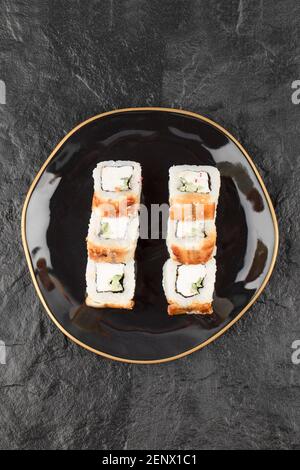 Schwarzer Teller mit Drachen-Sushi-Rollen mit Aal auf Schwarz Oberfläche Stockfoto