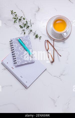 Flacher Schreibtisch mit Schreibtisch - eine Tasse Tee, mit Kommunikationsgerät und Schreibgeräten. Feminine Business Mockup, Copyspace, weißer Hintergrund. Stockfoto