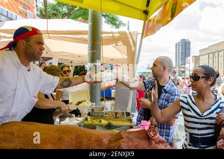 Salsa auf St. Saint Clair Festival Szenen: Ein Koch in einem Kopf-Tuch übergibt einen Behälter mit Lebensmitteln an einen Mann mit einem rasierten Kopf zur gleichen Zeit, dass h Stockfoto