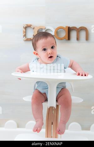 Lächelndes sechs Monate altes Baby sitzt in einem Hochstuhl Fütterung. Baby Fütterung. Baby Lernen. Stockfoto