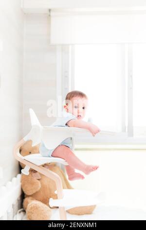 Lächelndes sechs Monate altes Baby sitzt in einem Hochstuhl Fütterung. Baby Fütterung. Baby Lernen. Stockfoto