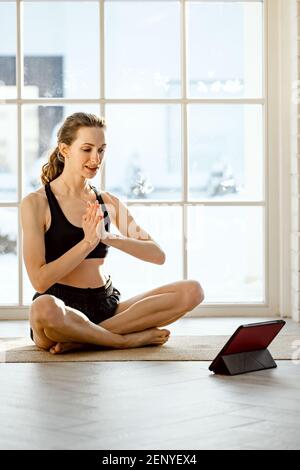 Yoga-Lehrer führt virtuelle Yoga-Klasse zu Hause auf einer Videokonferenz. Schöne fit Frau üben Online-Yoga mit Tablet. Heimfitness und wor Stockfoto