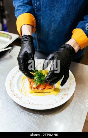 Der Koch hält einen Teller Toast mit pochiertem Ei, Lachs und Senfsoße auf weißem Hintergrund Stockfoto