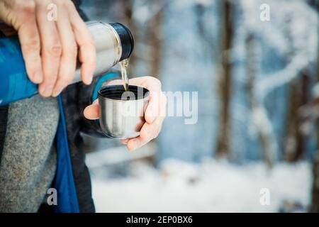 Mann gießt heißen Tee im Winterwald Stockfoto