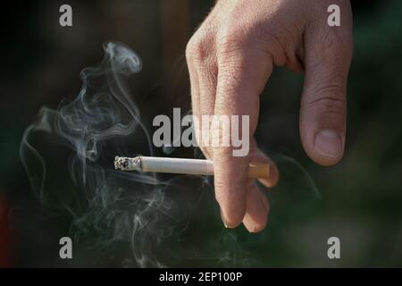 Mann Hand halten brennende Zigarette während des Rauchens, Tabakrauchsucht, ungesunder Lebensstil Stockfoto