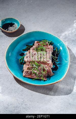 Rindertataki mit Sauce und Sesam auf blauem Teller. Japanisches Essen Stockfoto