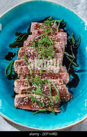 Rindertataki mit Sauce und Sesam auf blauem Teller. Japanisches Essen Stockfoto