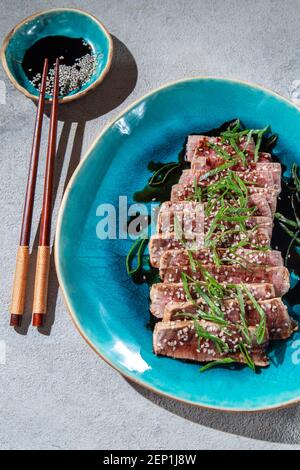 Rindertataki mit Sauce und Sesam auf blauem Teller. Japanisches Essen Stockfoto