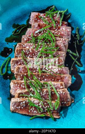 Rindertataki mit Sauce und Sesam auf blauem Teller. Japanisches Essen Stockfoto