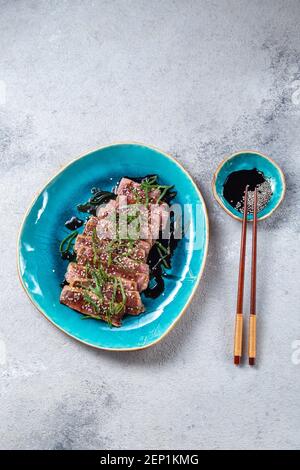 Rindertataki mit Sauce und Sesam auf blauem Teller. Japanisches Essen Stockfoto