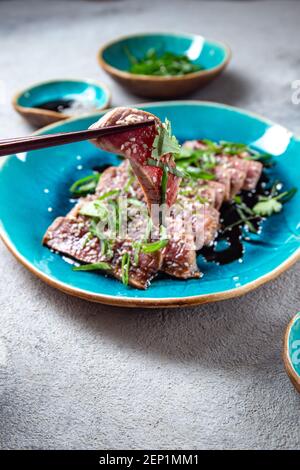 Rindertataki mit Sauce und Sesam auf blauem Teller. Japanisches Essen Stockfoto