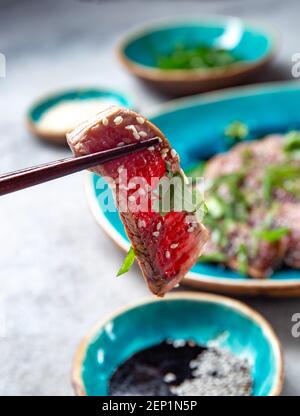 Rindertataki mit Sauce und Sesam auf blauem Teller. Japanisches Essen Stockfoto