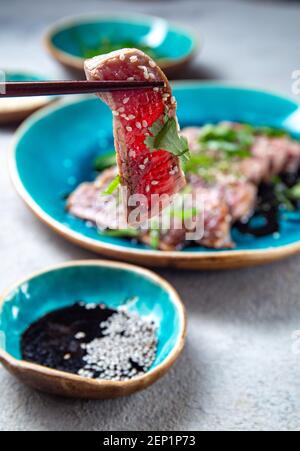 Rindertataki mit Sauce und Sesam auf blauem Teller. Japanisches Essen Stockfoto