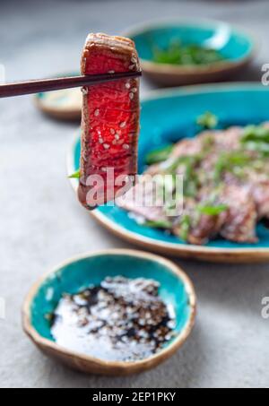 Rindertataki mit Sauce und Sesam auf blauem Teller. Japanisches Essen Stockfoto