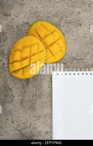 Mango mit Würfeln und leerem Notizbuch auf Marmoroberfläche Stockfoto