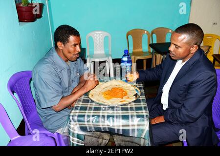 Äthiopier genießen ein traditionelles Injera-Gericht mit verschiedenen Gemüsesorten und Saucen. Stockfoto