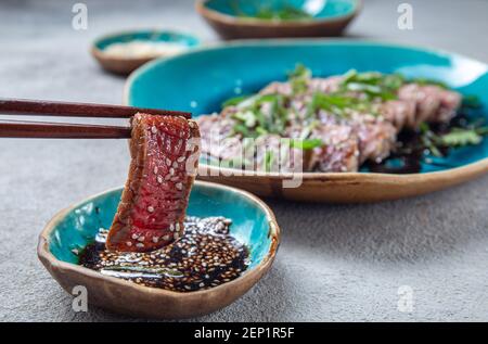 Rindertataki mit Sauce und Sesam auf blauem Teller. Japanisches Essen Stockfoto