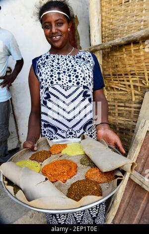 Eine äthiopische Kellnerin präsentiert ein traditionelles Injera-Gericht mit verschiedenen Gemüsesorten und Saucen. Stockfoto