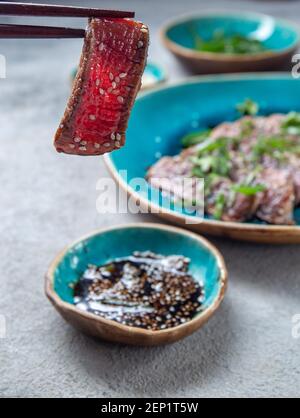Rindertataki mit Sauce und Sesam auf blauem Teller. Japanisches Essen Stockfoto