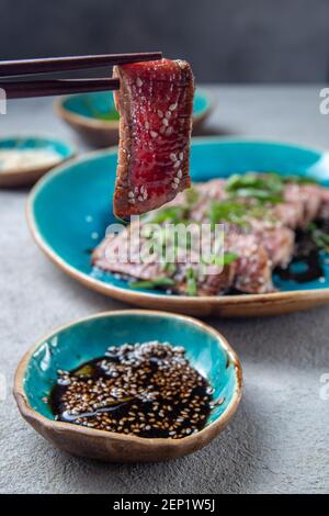 Rindertataki mit Sauce und Sesam auf blauem Teller. Japanisches Essen Stockfoto
