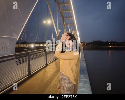 Nachts posiert eine junge Frau auf einer modernen Brücke. Stockfoto