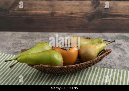 Köstliche fuyu-Kaki und reife Birnen im Weidenkorb Stockfoto