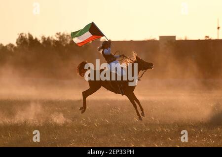 Peking, Kuwait. Februar 2021, 25th. Ein Mann, der eine kuwaitische Nationalflagge trägt, reitet ein Pferd während einer Reitausstellung in Mubarak Al-Kabeer Governorate, Kuwait, 25. Februar 2021. Kredit: Ghazy Qaffaf/Xinhua/Alamy Live Nachrichten Stockfoto