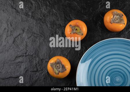 Blauer Teller mit köstlichen reifen fuyu-Kaki auf schwarzer Oberfläche Stockfoto