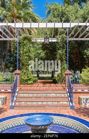 Schöne und traditionelle andalusische Terrasse mit einem Brunnen in der Mitte, Orangenbäume rund um den Brunnen, geflieste Sitze und ein Pavillon mit Pflanzen Stockfoto
