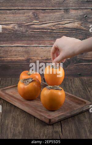 Weibliche Hand, die einzelne Kaki-Frucht auf Holzoberfläche nimmt Stockfoto