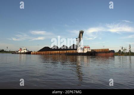 Ein Lastkahn wird an einer Tankstelle am Ufer des Mahakam-Flusses in der Provinz Ost-Kalimantan, Indonesien, mit Kohle beladen. Stockfoto