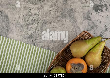 Köstliche fuyu-Kaki und reife Birnen im Weidenkorb Stockfoto