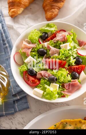 Gesunder Salat in einer Schüssel mit Oliven, Radgerichten, Tomaten, Käse und magerem Schinken zum Frühstück serviert Stockfoto