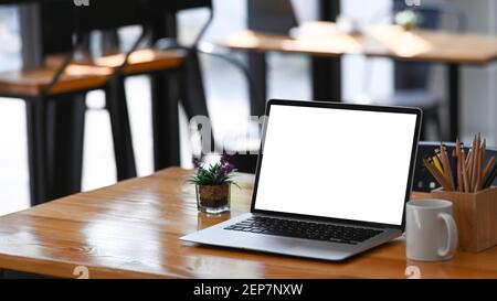 Offener Computer Laptop mit leerem Bildschirm, Kaffeetasse, Pflanze und Schreibwaren auf Holztisch. Stockfoto
