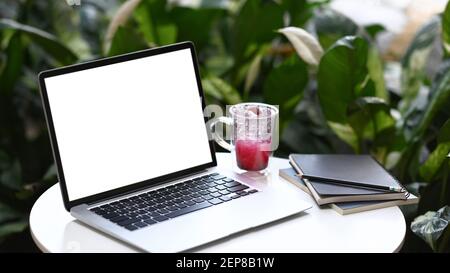 Nahaufnahme des Computers Laptop mit leerem Bildschirm, Notebook und Tasse frischen Getränken auf weißem Schreibtisch im Café. Stockfoto