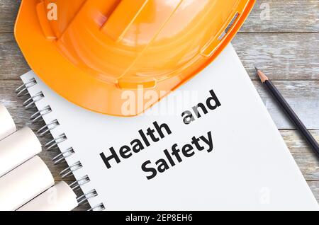 Gesundheit und Sicherheit mit orangefarbenem Helm, Bleistift und Notizbüchern auf Holztisch am Büroarbeitsplatz. Stockfoto