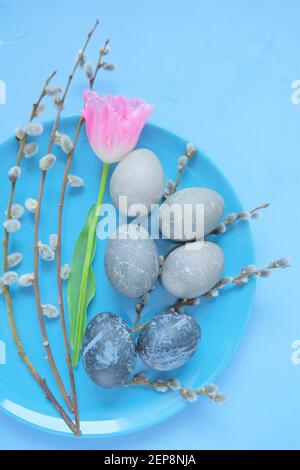 Osterferien.Ostern Marmor graue Eier, Weidenzweige und rosa Tulpenblume in einem blauen Teller auf blauem Hintergrund. Osteressen. Frühling religiösen Feiertag Stockfoto