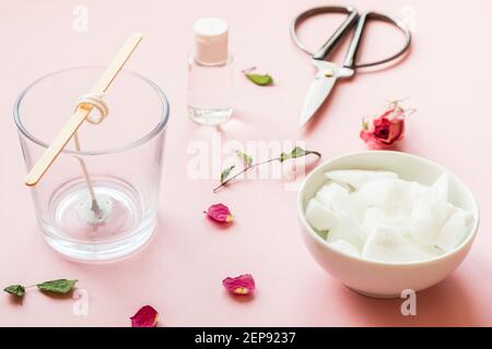 DIY-Konzept. Wachs, Docht, trockene Rosen - Zutaten für die Herstellung von handgefertigten Kerzen auf rosa Hintergrund Stockfoto