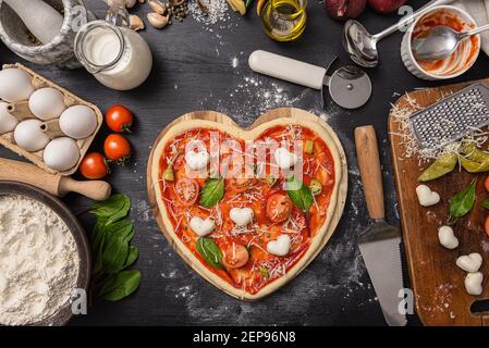 Frau bereitet ein festliches Abendessen für zwei zu Ehren von Valentinstag klassische italienische Pizza Margherita in Form von Ein Herz und Mozzarella im sh Stockfoto