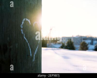 Herz gezeichnet mit weißer Kreide auf Strommast mit Sonne scheint und Schnee im Hintergrund. Stockfoto