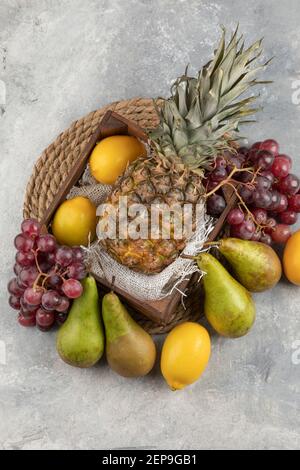Reife Ananas in Holzkiste mit verschiedenen frischen Früchten auf Marmoroberfläche Stockfoto