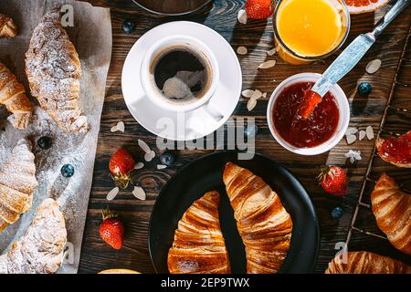 Das Konzept eines großen und abwechslungsreichen Frühstück. Verschiedene Croissants und Marmeladen, Kaffee und Amelsin Saft, Grapefruit und Erdbeeren auf der Tischplatte vie Stockfoto